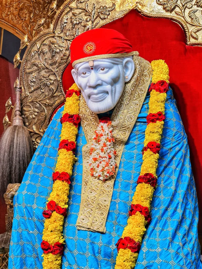 Sai Baba Statue Dressed in Bright Clothes Adorned with Flower Wreath