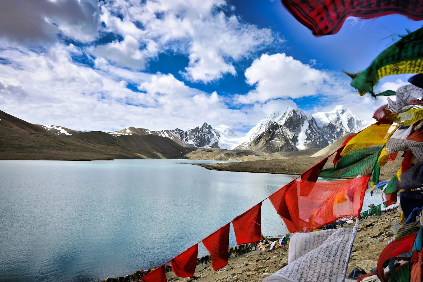 assorted flags on beach shore near snow covered mountains under blue and white sunny cloudy sky