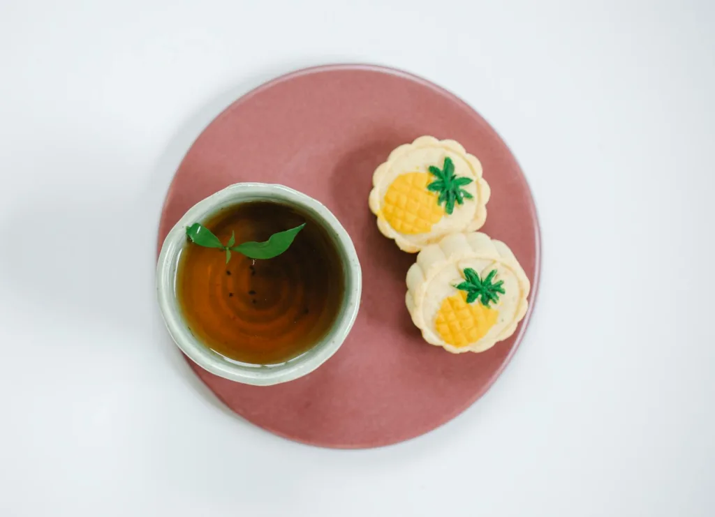 Top view of oriental cup of fresh tea with fresh mint leaves on plate with delicious pastries on light background