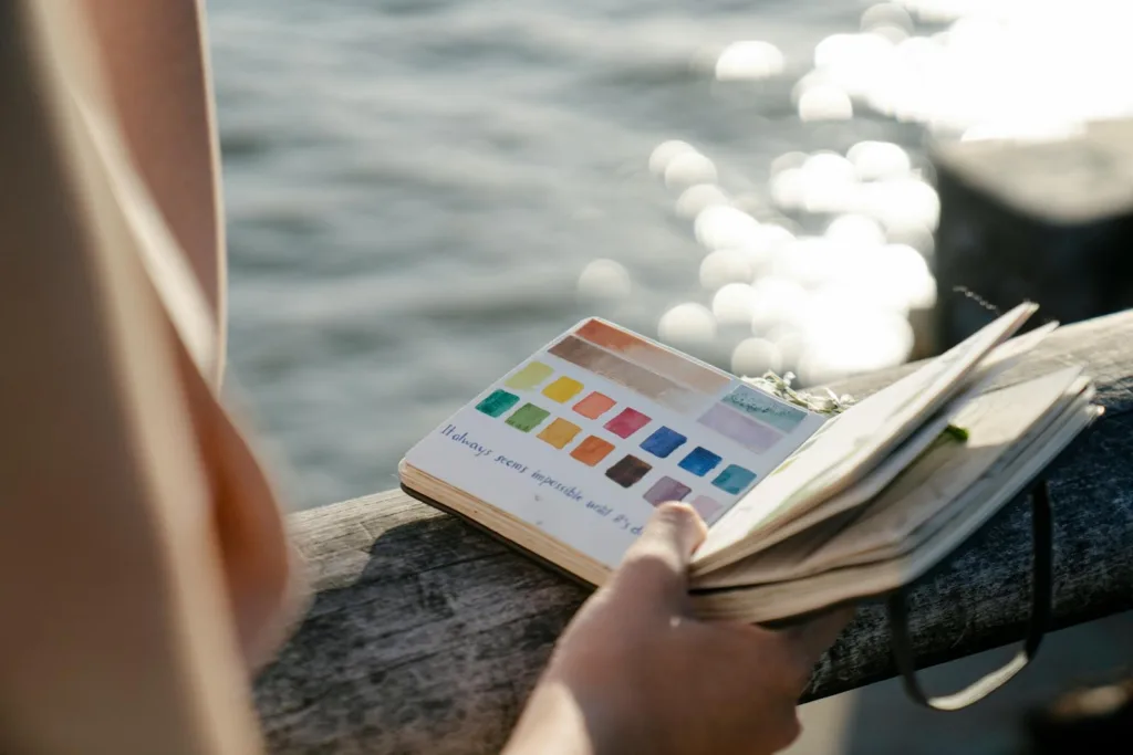 Crop artist with painted spectrum in notebook