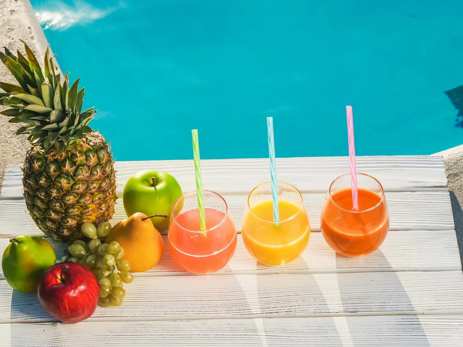 Fruits and Fruit Drinks with Straws in a Row by a Swimming Pool